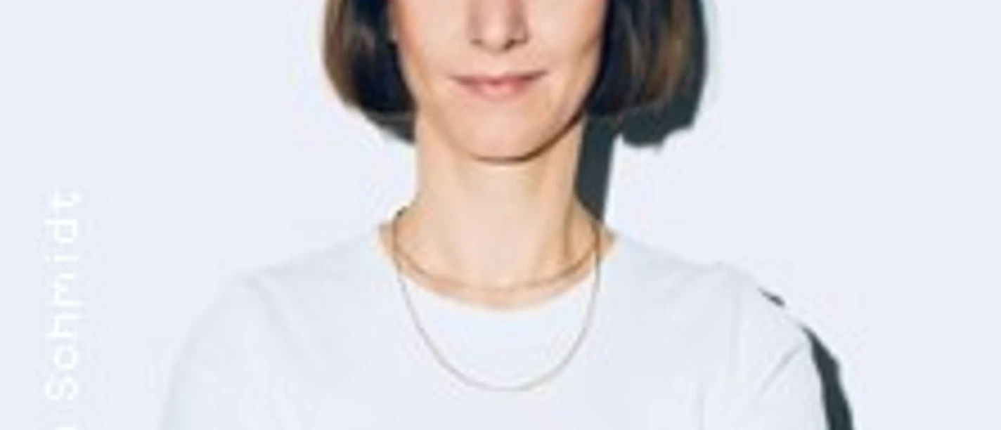 Frau mit kurzem Bob, weißem T-Shirt und tätowierten Armen steht mit verschränkten Armen.