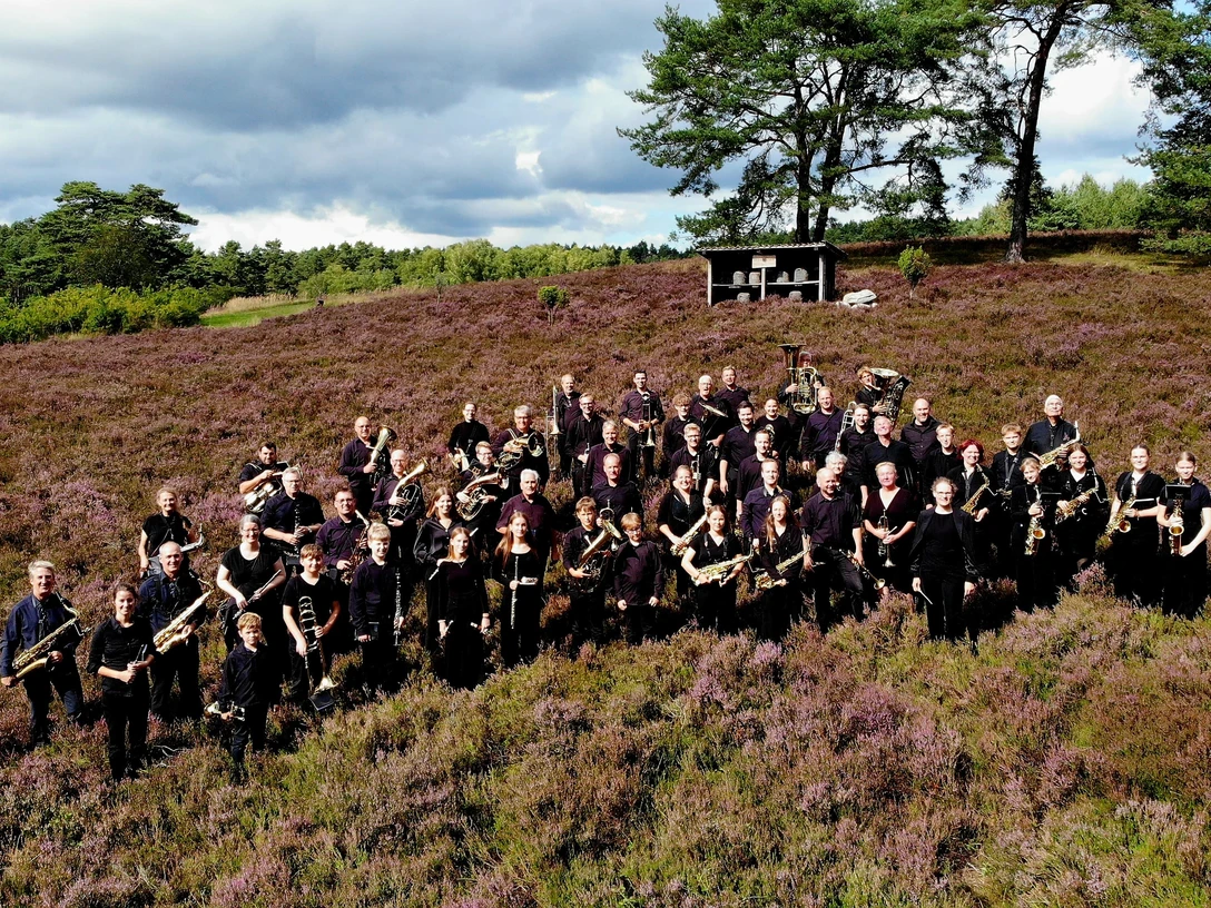 Blasorchester MTV Amelinghausen Menschen mit Blasinstrumenten stehen in lila Heide. Sie tragen dunkle Kleidung.