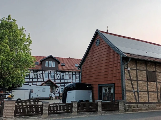 Salzgitter-Beinum_Pension_Wollschlaeger_HD_16zu9.jpg Fachwerkhaus mit rotem Ziegeldach, Innenhof, parkenden Fahrzeugen und angrenzender Scheune