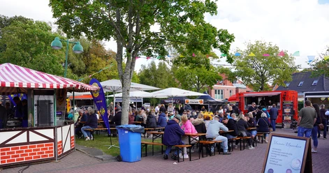 Street Food Festival Greetsiel Menschen sitzen an Holzbänken zwischen Foodtrucks und bunten Fahnen beim Street Food Festival.