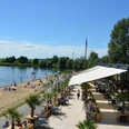 Salzgitter_Cafedellago_HD_16zu9.JPG Restaurantterrasse am Seeufer mit Gästen, Strandbereich und Badenden unter blauem Himmel