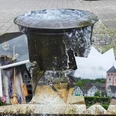 Hexenohnder Brunnen mit einer Hexenfigur, umgeben von Fachwerkhäusern und dem Turm der Kirche St. Pankratius.