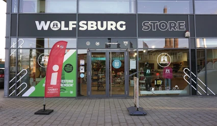 Glasfassade des Wolfsburg Store mit Eingang zur Tourist-Information und Aufsteller im Vordergrund