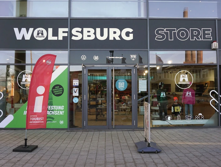 Glasfassade des Wolfsburg Store mit Eingang zur Tourist-Information und Aufsteller im Vordergrund