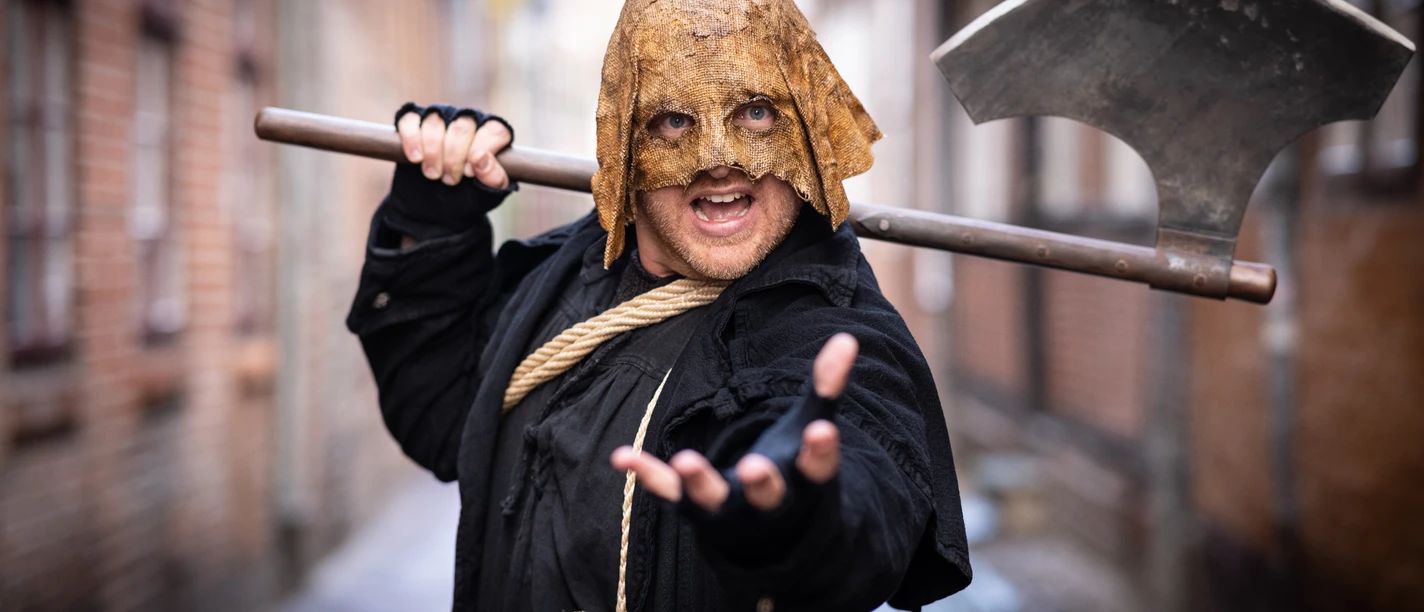Lüneburger Henker_CC BY-SA_©Verein Lüneburger Stadtführer.jpg Mann im Henkersgewand mit großer Axt und Sackmaske steht in einer engen Lüneburger Gasse.