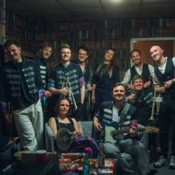 Musikgruppe mit Instrumenten in einem Raum, locker zusammenstehend vor einem Bücherwandmotiv