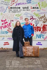 Theaterplakat zu Leonce und Lena Zwei Personen stehen vor einer mit Graffiti bemalten Wand. Zwei alte Lederkoffer stehen vor ihren Füßen.