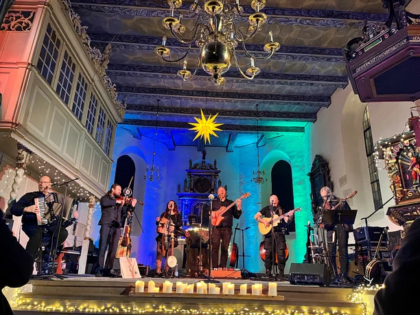 Band spielt in farbig beleuchteter Kirche vor Altar, Kerzen und Herrnhuter Stern.