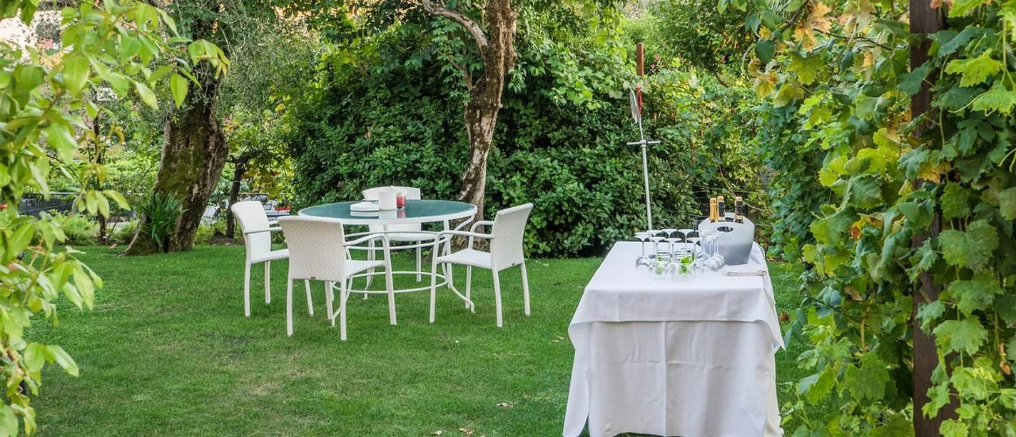 Weißes Dinner Wingst Weiß gedeckter Tisch im Grünen mit Gläsern und Flaschen, umgeben von Bäumen und sommerlichem Licht