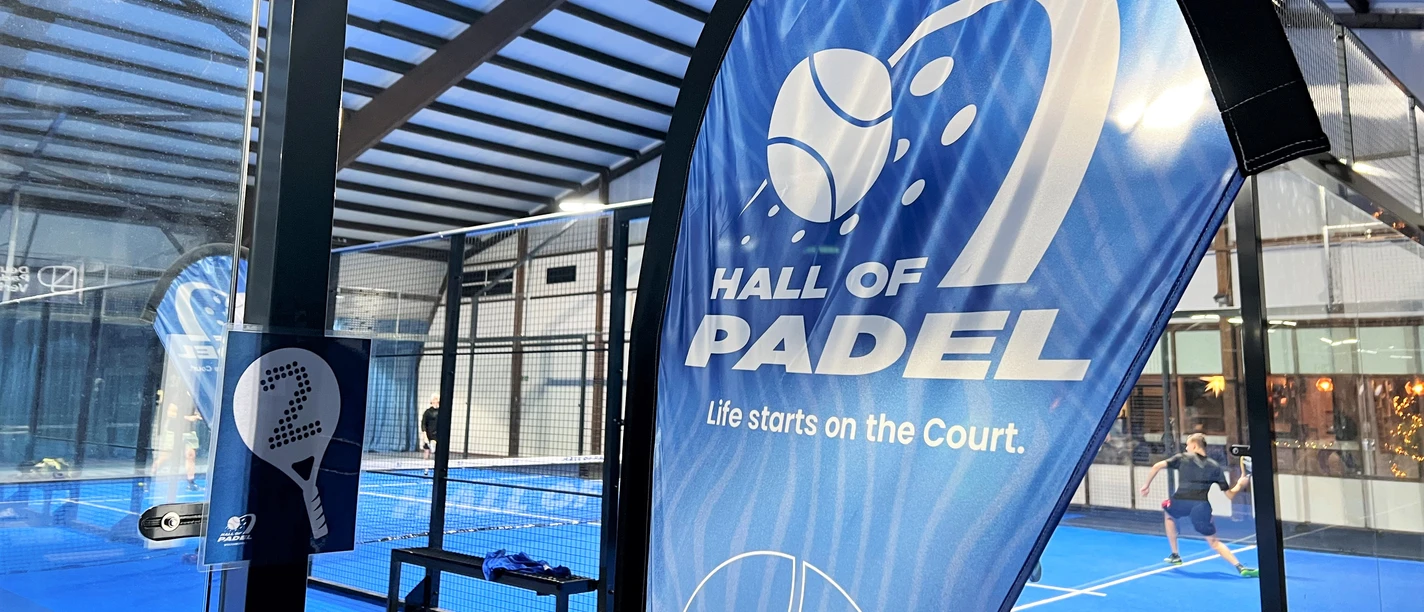 Hall of Padel Innenansicht einer modernen Padelhalle mit blauem Spielfeld und spielenden Personen im Hintergrund