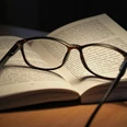 Lesung Aufgeschlagenes Buch mit Lesebrille in warmem Licht, Sinnbild für Literaturgenuss und Inspiration.