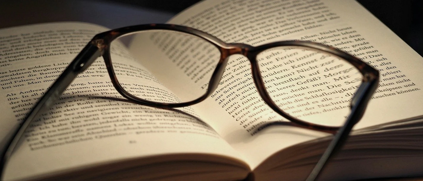 Lesung Aufgeschlagenes Buch mit Lesebrille in warmem Licht, Sinnbild für Literaturgenuss und Inspiration.