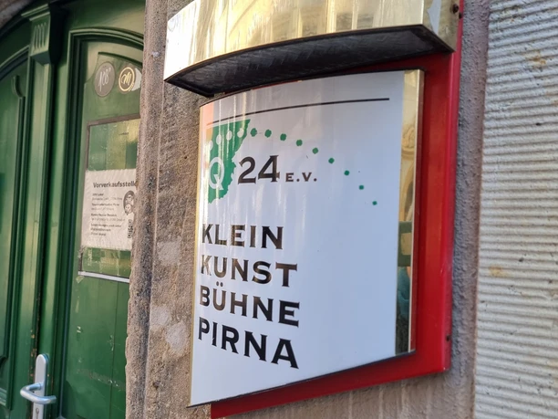 Schild Kleinkunstbühne an Hauswand dahinter grüne Eingangstür
