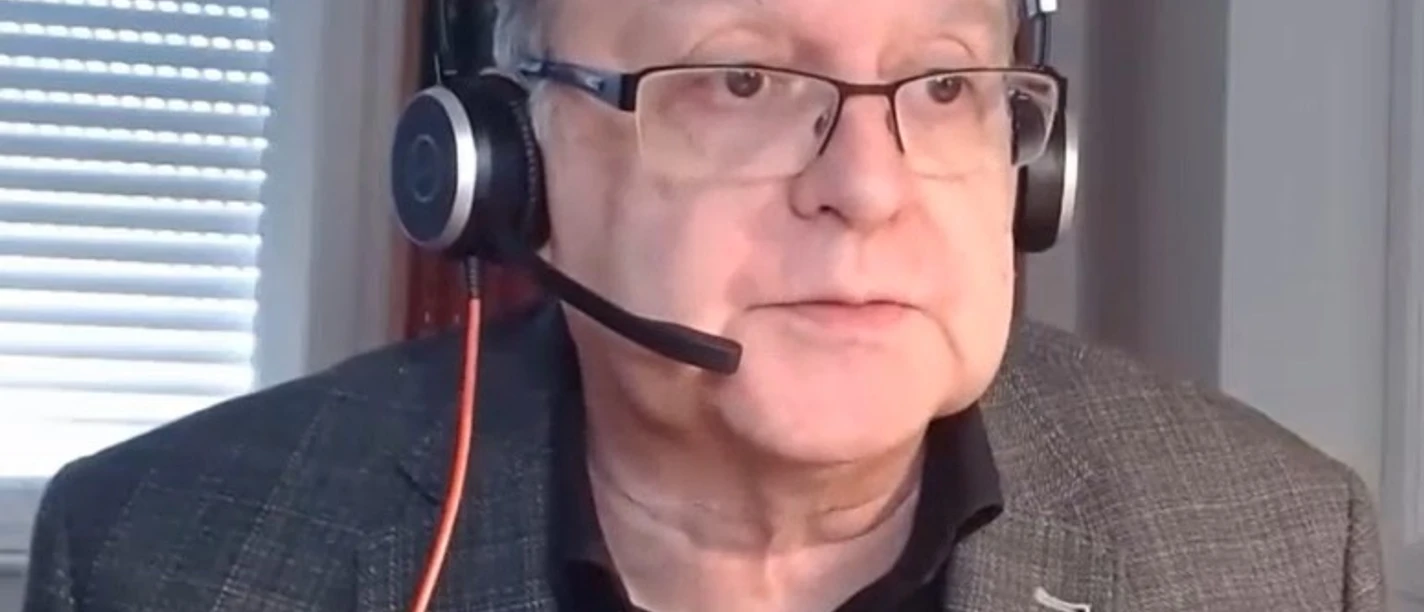 Autorenfoto_Welchering.jpg Mann mit grauem Sakko, schwarzem Hemd und Kopfhörern vor einem Bücherregal und einem Fenster mit Jalousien