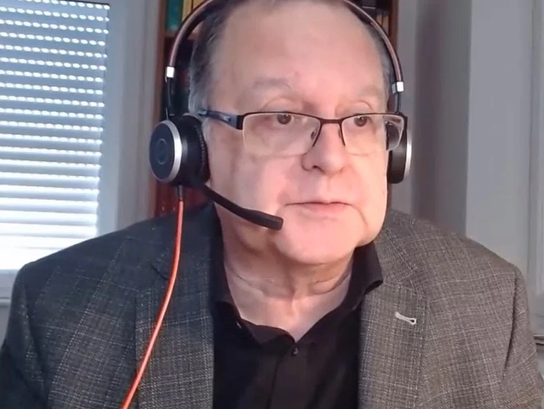 Autorenfoto_Welchering.jpg Mann mit grauem Sakko, schwarzem Hemd und Kopfhörern vor einem Bücherregal und einem Fenster mit Jalousien