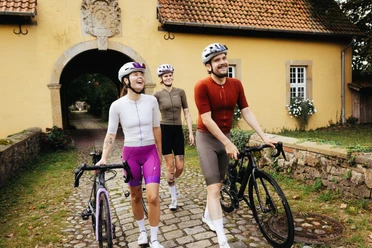 Unterwegs am Kloster Malgarten in Bramsche Drei Rennradfahrende schieben ihre Räder durch den Torbogen des Kloster Malgarten, umgeben von historischer Klosterarchitektur.