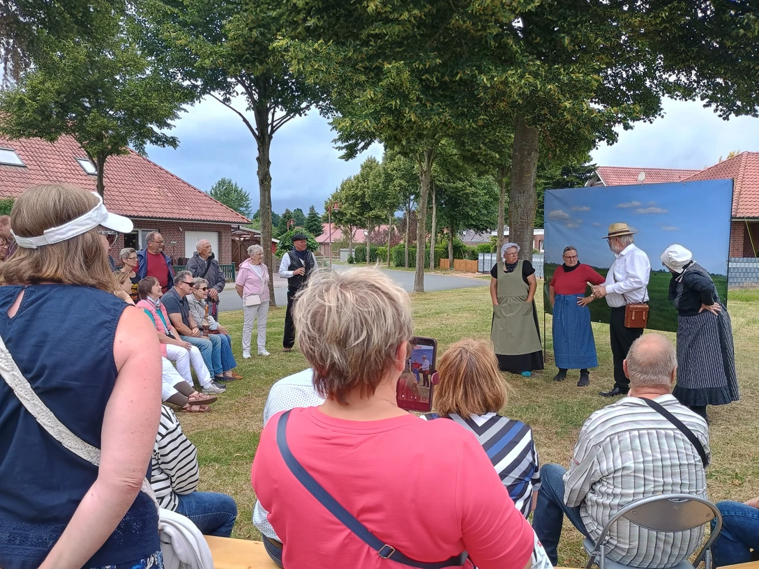FehnTheater.jpg Gruppe von Menschen sitzt und steht im Freien vor drei Personen in historischer Kleidung, die eine Szene aufführen