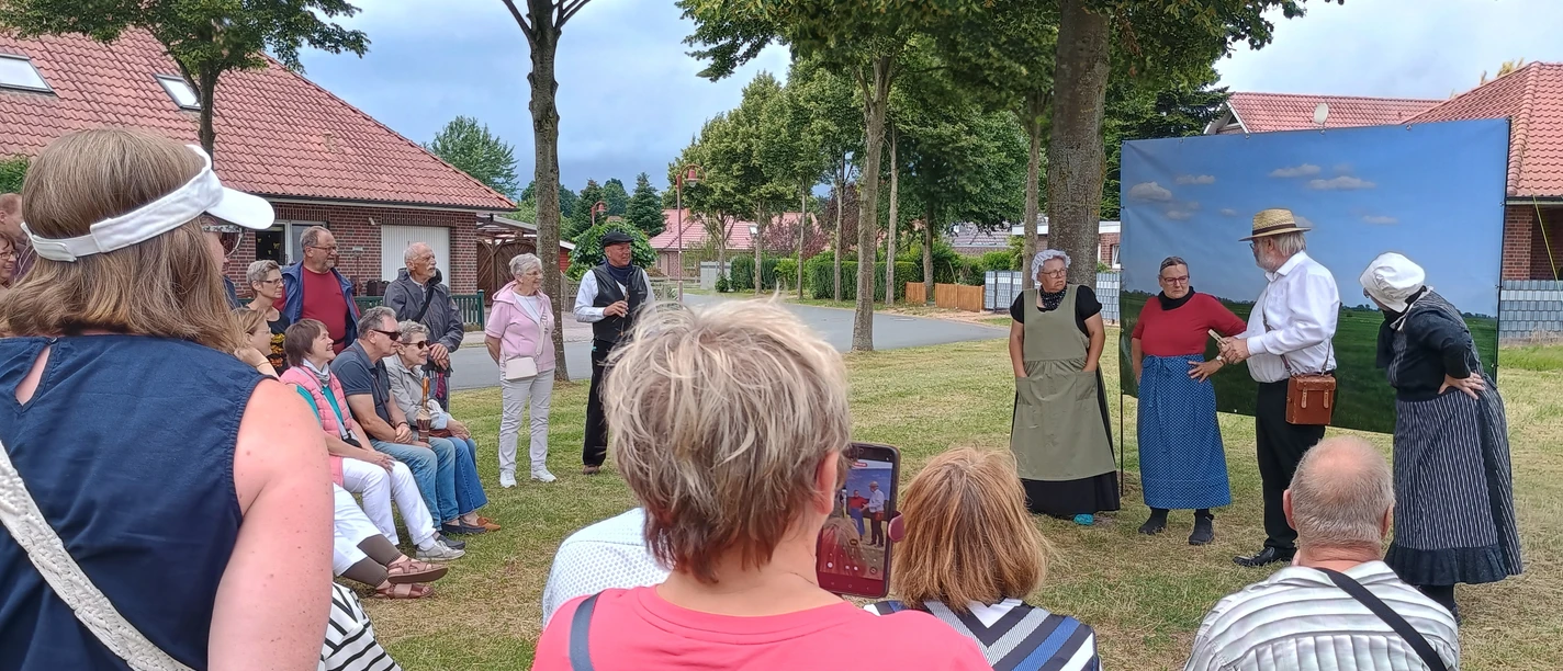 FehnTheater.jpg Gruppe von Menschen sitzt und steht im Freien vor drei Personen in historischer Kleidung, die eine Szene aufführen