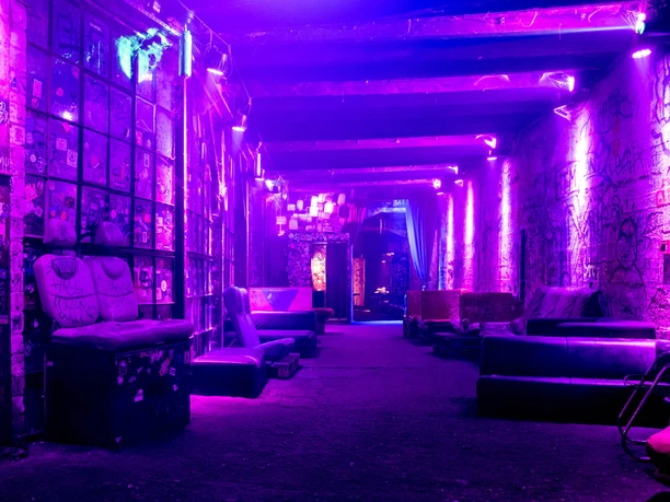 Odonien Violett beleuchteter Industriegang mit Graffitwänden und abgenutzten Sitzmöbeln.
