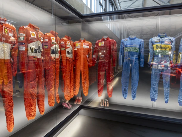 MOTORWORLD Cologne Rhineland Racing suits of various teams in an illuminated glass display case of an exhibition.
