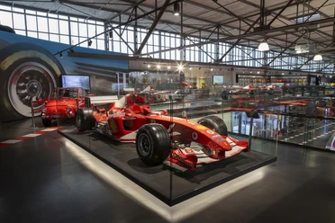 MOTORWORLD Cologne Rhineland Red Formula 1 car in a modern exhibition hall with glass showcases and other vehicles.