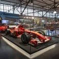 MOTORWORLD Cologne Rhineland Red Formula 1 car in a modern exhibition hall with glass showcases and other vehicles.