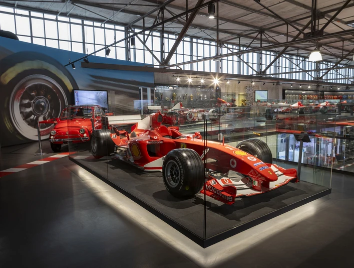 MOTORWORLD Köln Rheinland Roter Formel-1-Wagen in moderner Ausstellungshalle mit Glasvitrinen und weiteren Fahrzeugen.Red Formula 1 car in a modern exhibition hall with glass showcases and other vehicles.