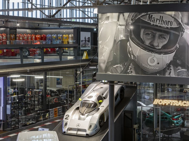 MOTORWORLD Köln Rheinland Motorsporthalle mit Rennwagen, Vitrinen und großem Porträt von Michael Schuhmacher im Ausstellungsraum.