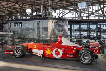Michael Schumacher Private Collection Roter Formelwagen in verglaster Ausstellungshalle mit großformatigen Fotos von Michael Schuhmacher im Hintergrund