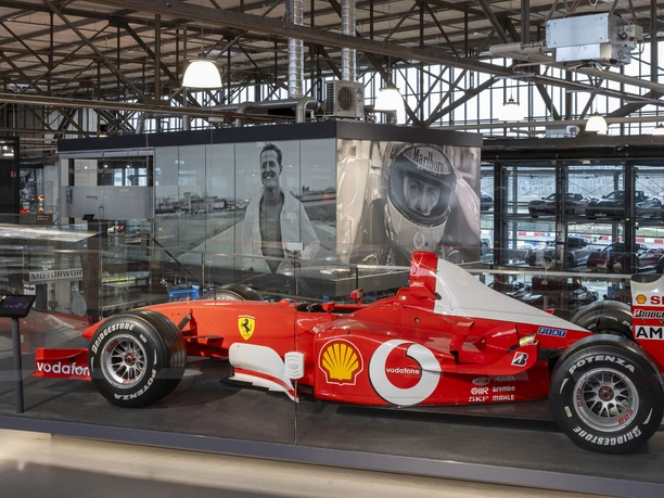 Michael Schumacher Private Collection Red formula car in glazed exhibition hall with large-format photos of Michael Schuhmacher in the background