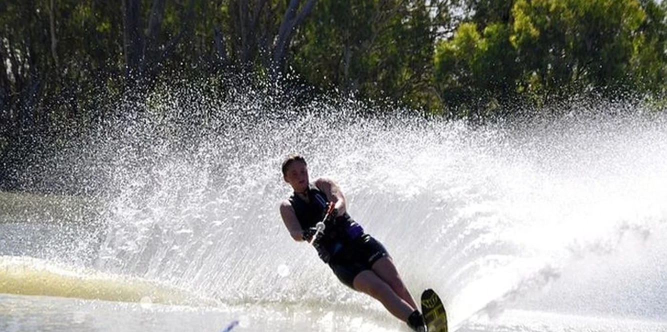 Wasserski Wassersportler gleitet mit Wasserskiern über glänzendes Wasser, umgeben von sprühender Gischt