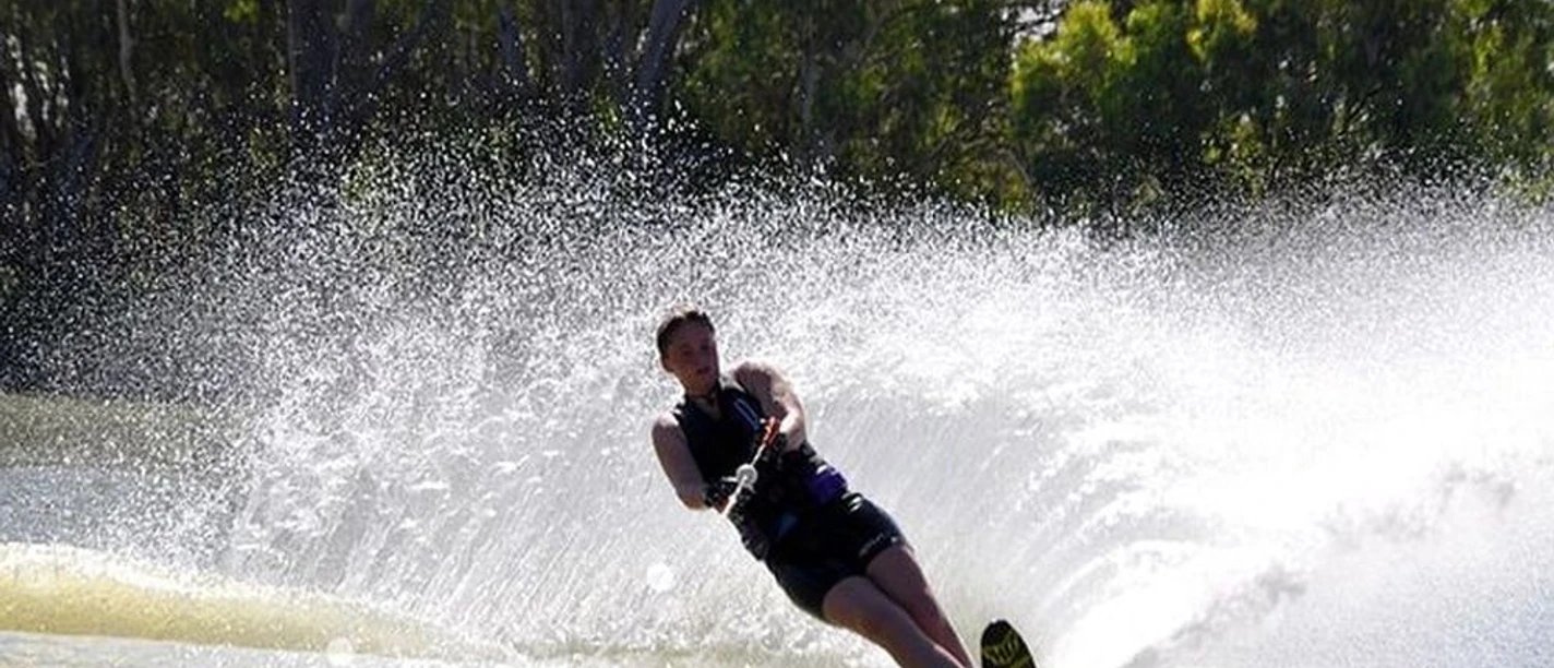 Wasserski Wassersportler gleitet mit Wasserskiern über glänzendes Wasser, umgeben von sprühender Gischt