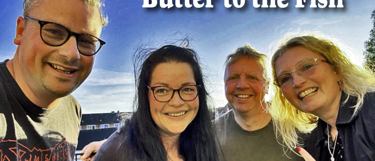 Butter to the Fish.jpg Vier Bandmitglieder von Butter to the Fish lächelnd im Freien unter blauem Himmel.