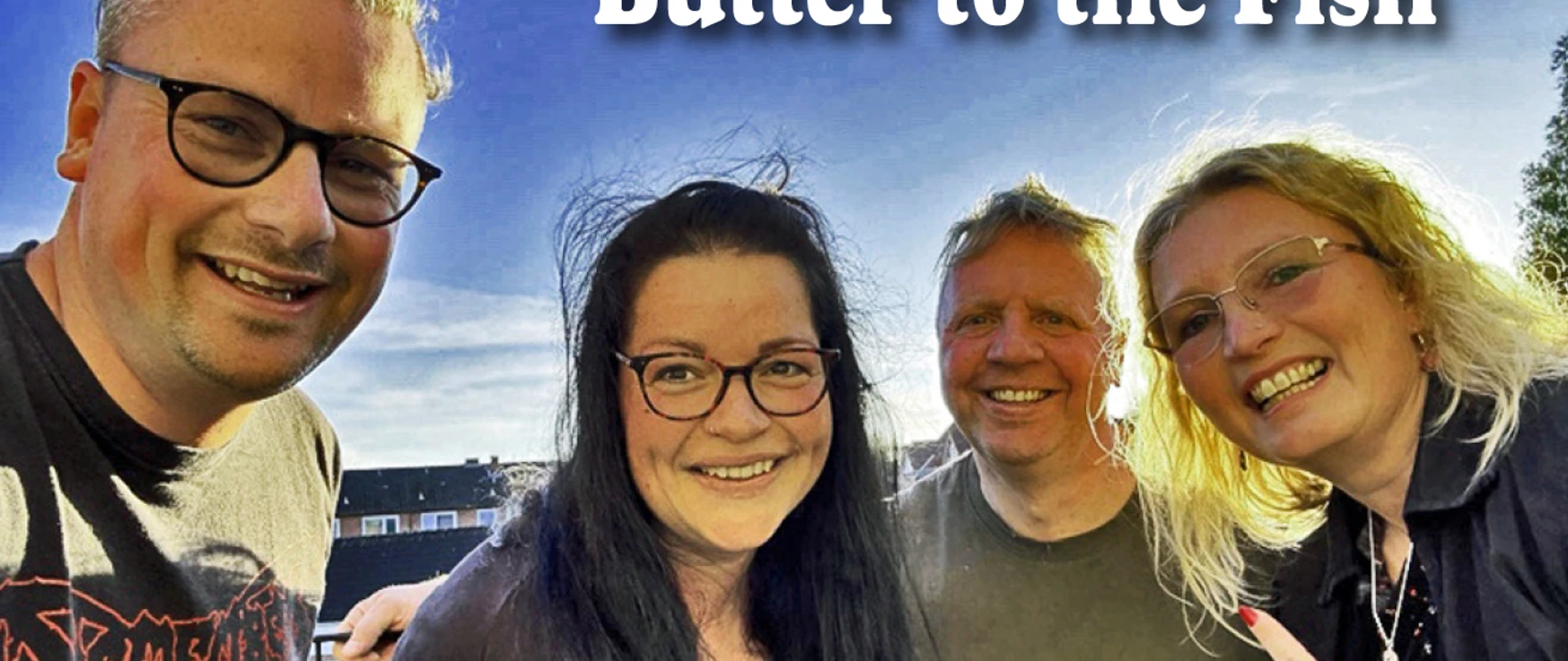 Butter to the Fish.jpg Vier Bandmitglieder von Butter to the Fish lächelnd im Freien unter blauem Himmel.