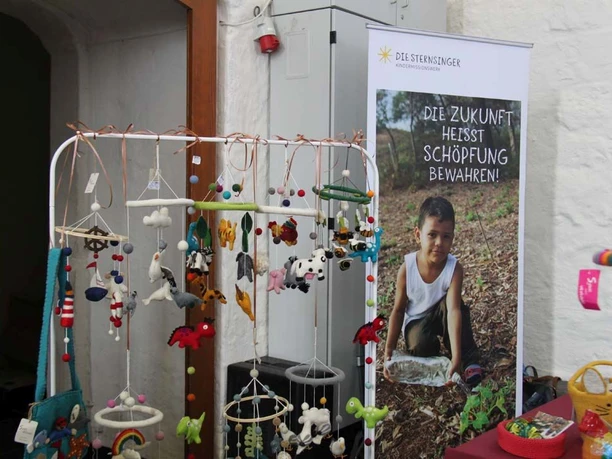 Fairtrade Messe 2024 (2) (c) Eine Welt Forum e.V..jpg An einem Messestand sind verschiedene, handgearbeitete Kinderspielzeuge und Anhänger ausgestellt.