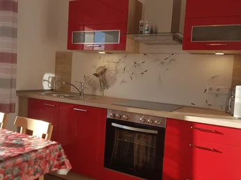 Helle Küche mit roten Schränken, Herd, Backofen, Spüle und Esstisch am Fenster