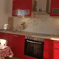 fewo_lebensfreude_kueche1 1.jpg Helle Küche mit roten Schränken, Herd, Backofen, Spüle und Esstisch am Fenster