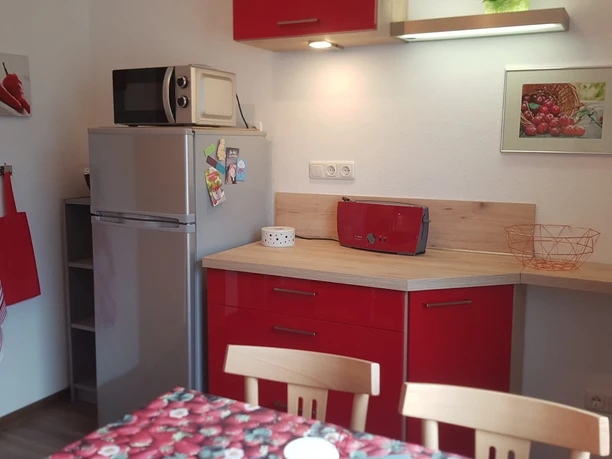 Kompakte Küche mit roten Schränken, Kühlschrank, Mikrowelle, Holzarbeitsplatte