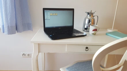 fewo_lebensfreude_schreibtisch.jpg Weißer kleiner Holzschreibtisch mit Laptop, Kaffeetasse und Thermoskanne