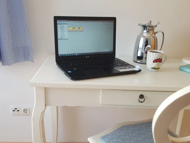 fewo_lebensfreude_schreibtisch.jpg Weißer kleiner Holzschreibtisch mit Laptop, Kaffeetasse und Thermoskanne