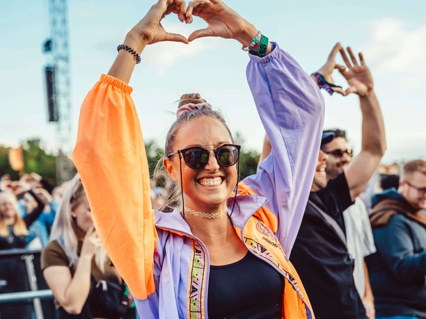 Rainbow Festival People celebrate outdoors, a person forms a heart with his hands in front of a blue sky