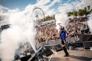 Rainbow Festival Stage shot with singing person, smoke and large festival crowd in front of Ferris wheel