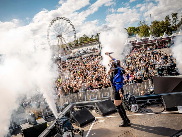 Rainbow Festival Stage shot with singing person, smoke and large festival crowd in front of Ferris wheel