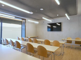 Bed & Sport Willisau Heller Seminarraum mit Holztischen und Holzstühlen, grossem Bildschirm und modernen Deckenleuchten