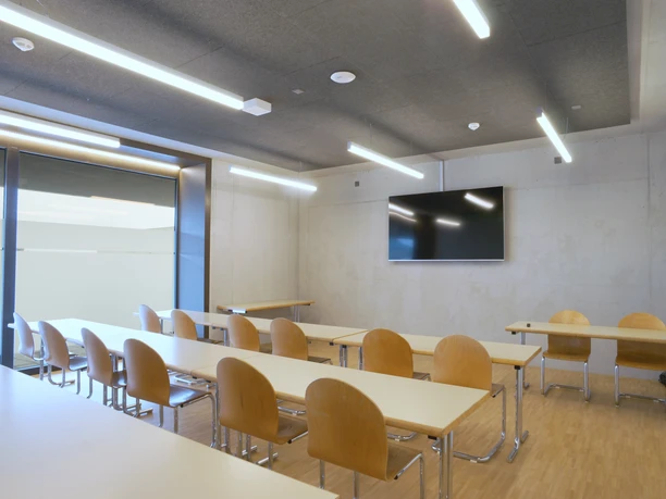 Bed & Sport Willisau Heller Seminarraum mit Holztischen und Holzstühlen, grossem Bildschirm und modernen Deckenleuchten