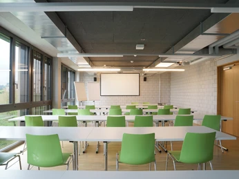 Bed & Sport Willisau Moderner Seminarraum mit grossen Fenstern, grünen Stühlen, langen Tischen und Projektionsleinwand