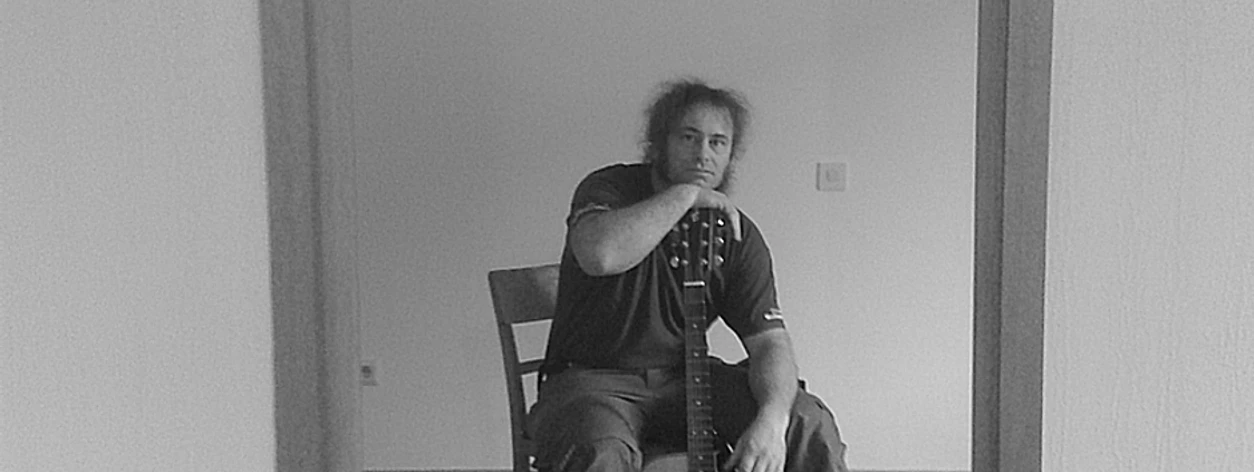 Stefan Keil.jpg Person sitzt auf einem Stuhl und hält eine Gitarre in der Hand