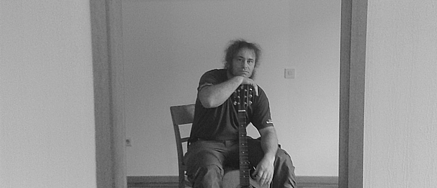 Stefan Keil.jpg Person sitzt auf einem Stuhl und hält eine Gitarre in der Hand