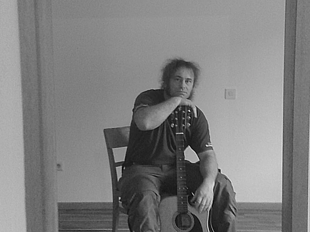 Stefan Keil.jpg Person sitzt auf einem Stuhl und hält eine Gitarre in der Hand