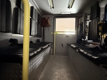 IMG_0803.jpg Innenraum eines Feuerwehrfahrzeugs mit gepolsterten Sitzbänken, Haltestangen und Ausrüstungen.